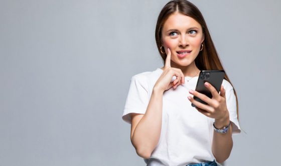 Portrait of a thoughtful doubtful asian woman talking on mobile phone and looking up over white background