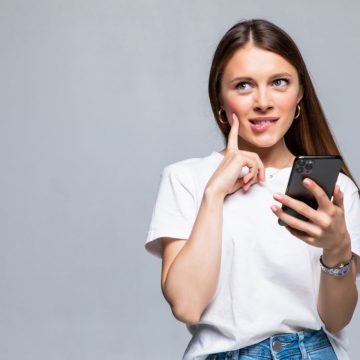 Portrait of a thoughtful doubtful asian woman talking on mobile phone and looking up over white background