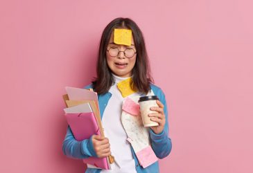 Overworked frustrated female accountant has much remote work surrounded with paper documents drinks coffee to go cries from despair isolated over pink background. Upset woman employee has problems